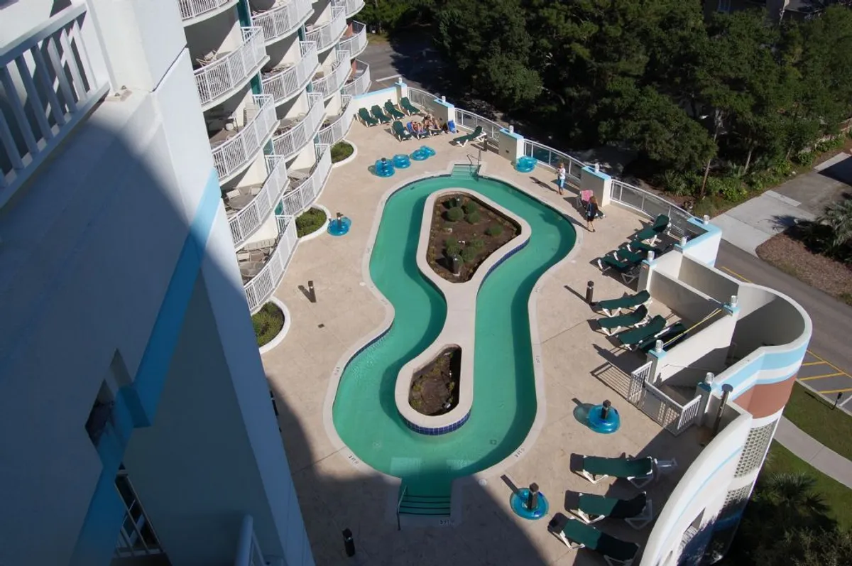 An inviting resort swimming pool surrounded by comfortable lounge chairs and lush landscaping. The pool deck is prepared for relaxation, sunbathing, and social gatherings, offering a welcoming atmosphere for guests to unwind together.