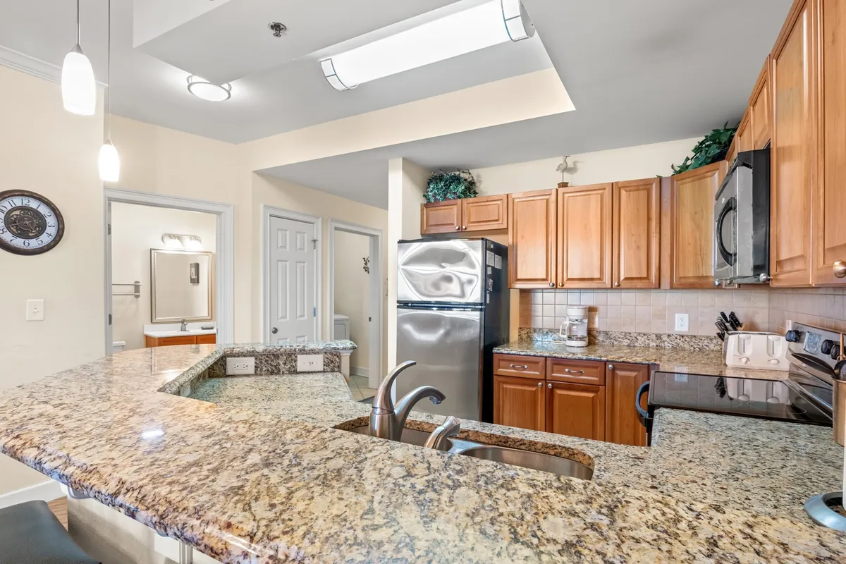 This inviting interior shot centers on a modern kitchen featuring a gleaming granite countertop, rich wood cabinetry, and stainless steel appliances. The space is clearly designed for both everyday cooking and entertaining, with ample prep area and a warm, welcoming vibe.