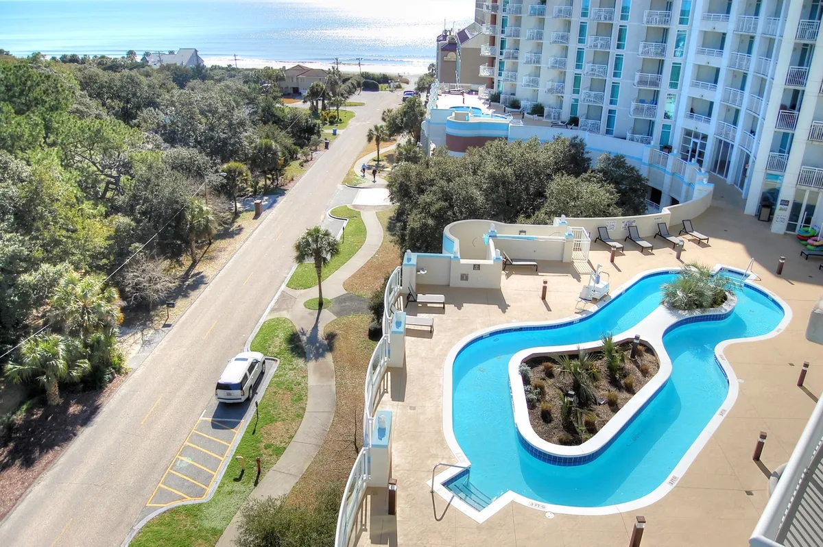 This image features a spacious outdoor pool area with views of the ocean, surrounded by greenery and lounge chairs. A road leads to the beach, creating a seamless connection between the resort's amenities and the seaside atmosphere. The scene captures guests swimming, sunbathing, and enjoying the relaxing coastal setting.