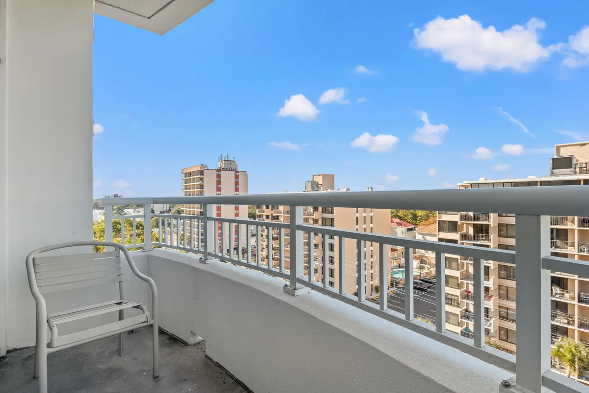 A serene exterior view from a private balcony with a simple chair overlooking the city skyline and stretches of coastline, suggesting peaceful morning routines such as enjoying coffee or reading while basking in the ocean air.