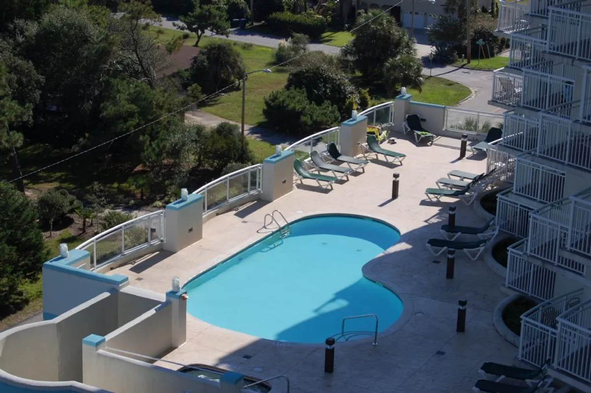 A vibrant swimming pool is surrounded by comfortable lounge chairs and lush greenery. The scene is lively yet relaxed, inviting guests to swim, sunbathe, or unwind poolside, embodying the leisurely atmosphere promised by the resort's amenities.